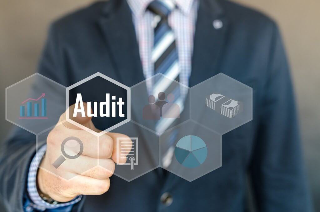 A cropped photo of a man in a suit pointing to a button that reads “audit.” | website content audit
